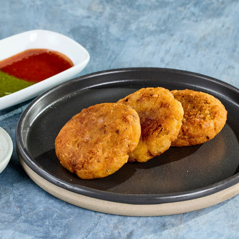 Three crisp aloo tikki on a dark plate with green and red chutney