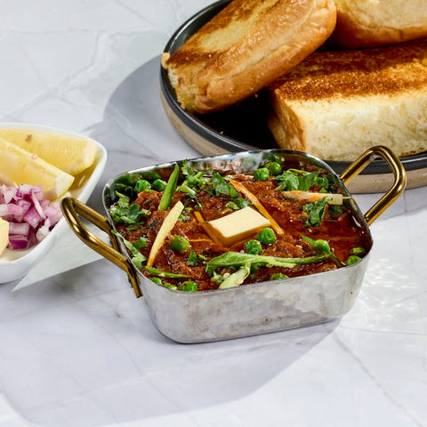 Pav bhaji topped with butter and coriander, with toasted pav, chopped onion and lemon