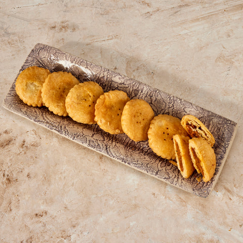 A row of round achari mathi on a grey platter