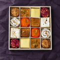 Top view of the Bring India Home box: Kesar Motichoor Ladoo, Gond Ladoo, Danedar Burfi, gold-wrapped Channa Burfi, Rose Badaam Ladoo, Kaju Jalebi, Milk Cake and Sangam Burfi