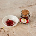 Deep red Pure Desi kesar saffron threads in a white dish beside the corked glass jar