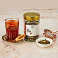 Pure Desi masala chai tea blend jar beside a glass of brewed chai, a mathi and a strainer