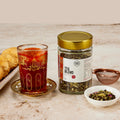 Pure Desi tea blend with a glass of chai, a plate of mathi and loose blend showing cardamom and rose petals