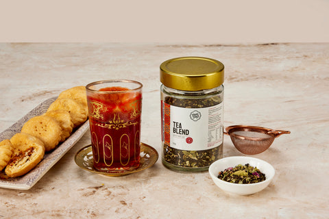 Pure Desi tea blend with a glass of chai, a plate of mathi and loose blend showing cardamom and rose petals